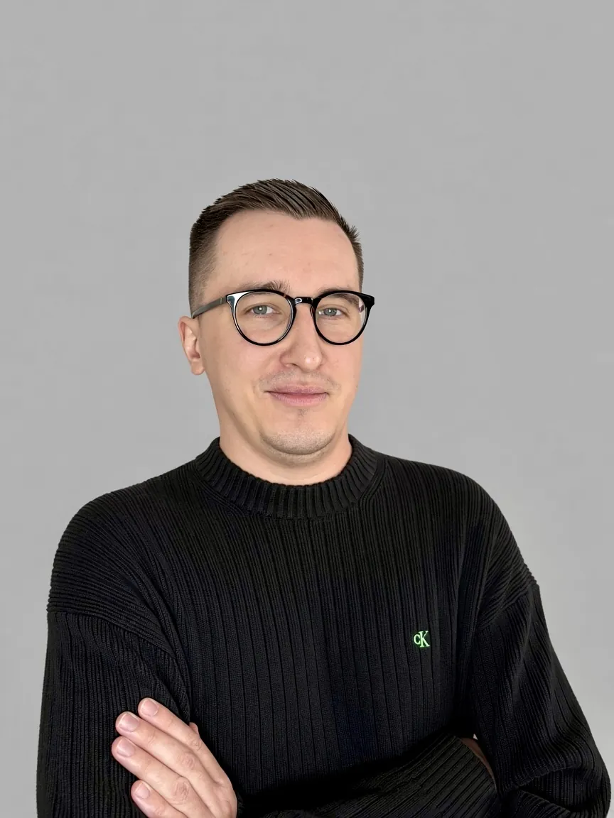 Michał Kansy w okularach i czarnym swetrze, na szarym tle